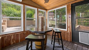 A covered outdoor area with a wooden ceiling, large windows, and a bar stool. - Pet Friendly! Hot Tub | Pool Table | Fire Pit (Pigeon Forge)