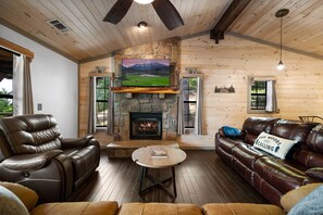 A cozy cabin interior with a stone fireplace, leather sofas, and a television mounted above it.