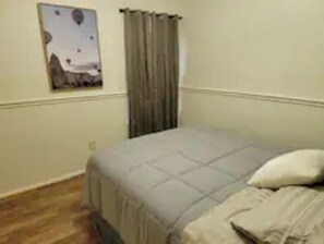 Simple bedroom with a single bed, wall art, and a window with a curtain.