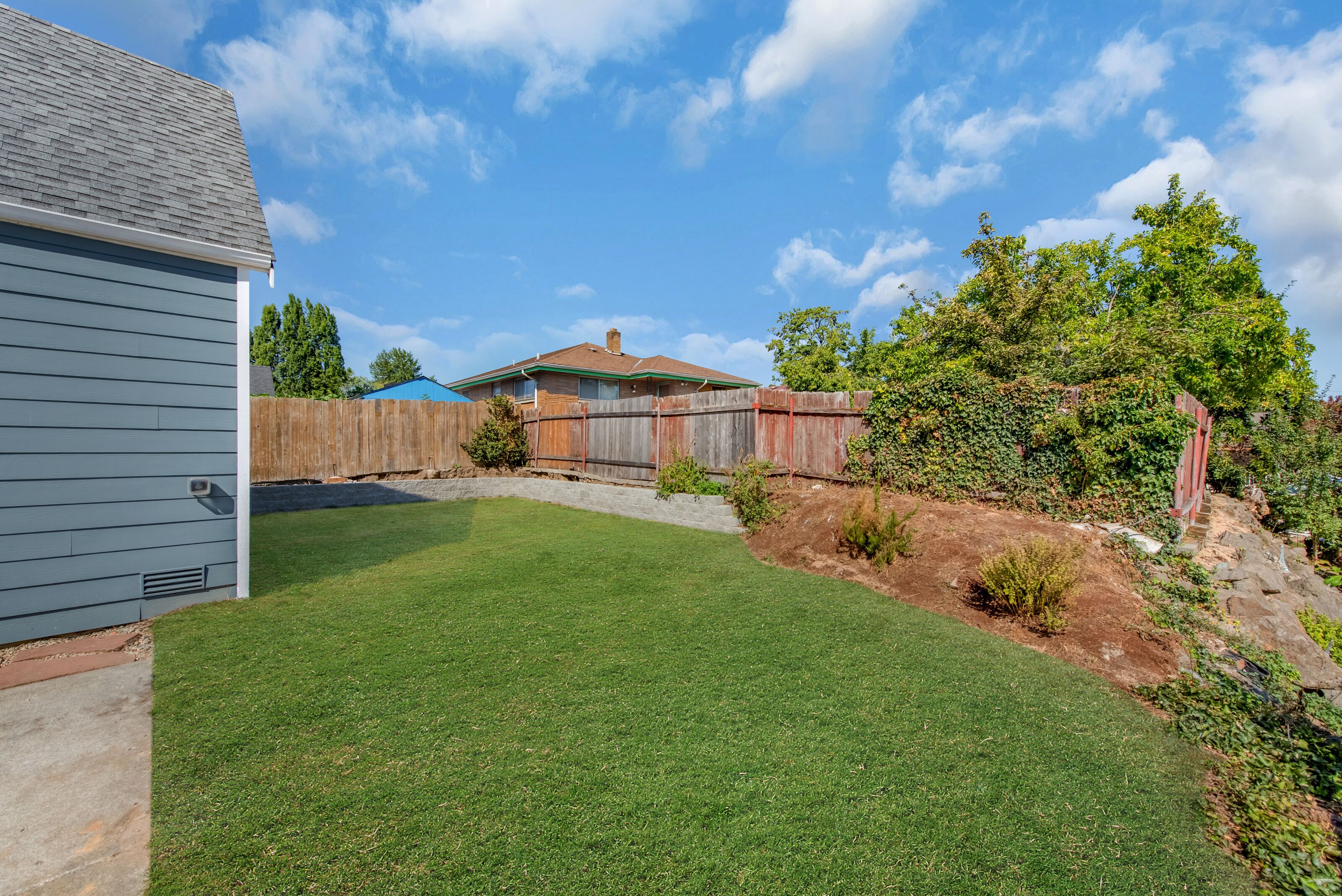 A backyard with a well-maintained lawn, a wooden fence, and a house with a brown roof.