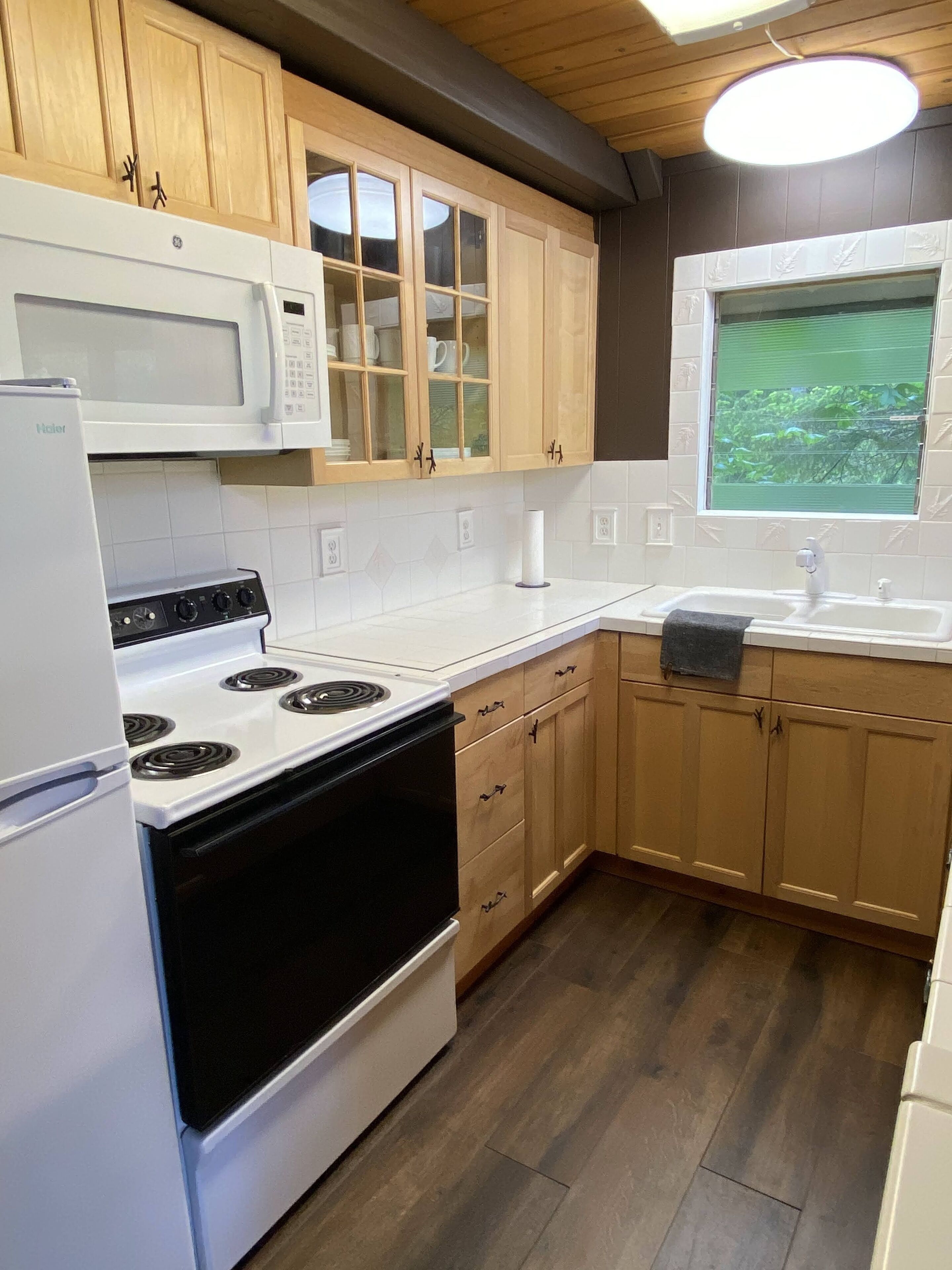 Una cocina con armarios de madera, una estufa blanca, un microondas y una ventana con vistas a zonas verdes.