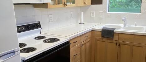 Una cocina con armarios de madera, una estufa blanca, un microondas y una ventana con vistas a zonas verdes.