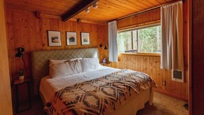 Une chambre aux murs lambrissés, avec un lit, des tableaux encadrés et une fenêtre avec des rideaux.