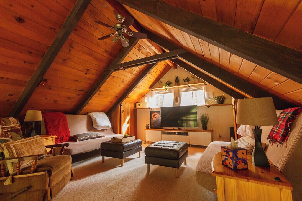 Een gezellig slaapkamer op zolder met een schuine kap, een bed, een bank, een televisie en een kitchenette.