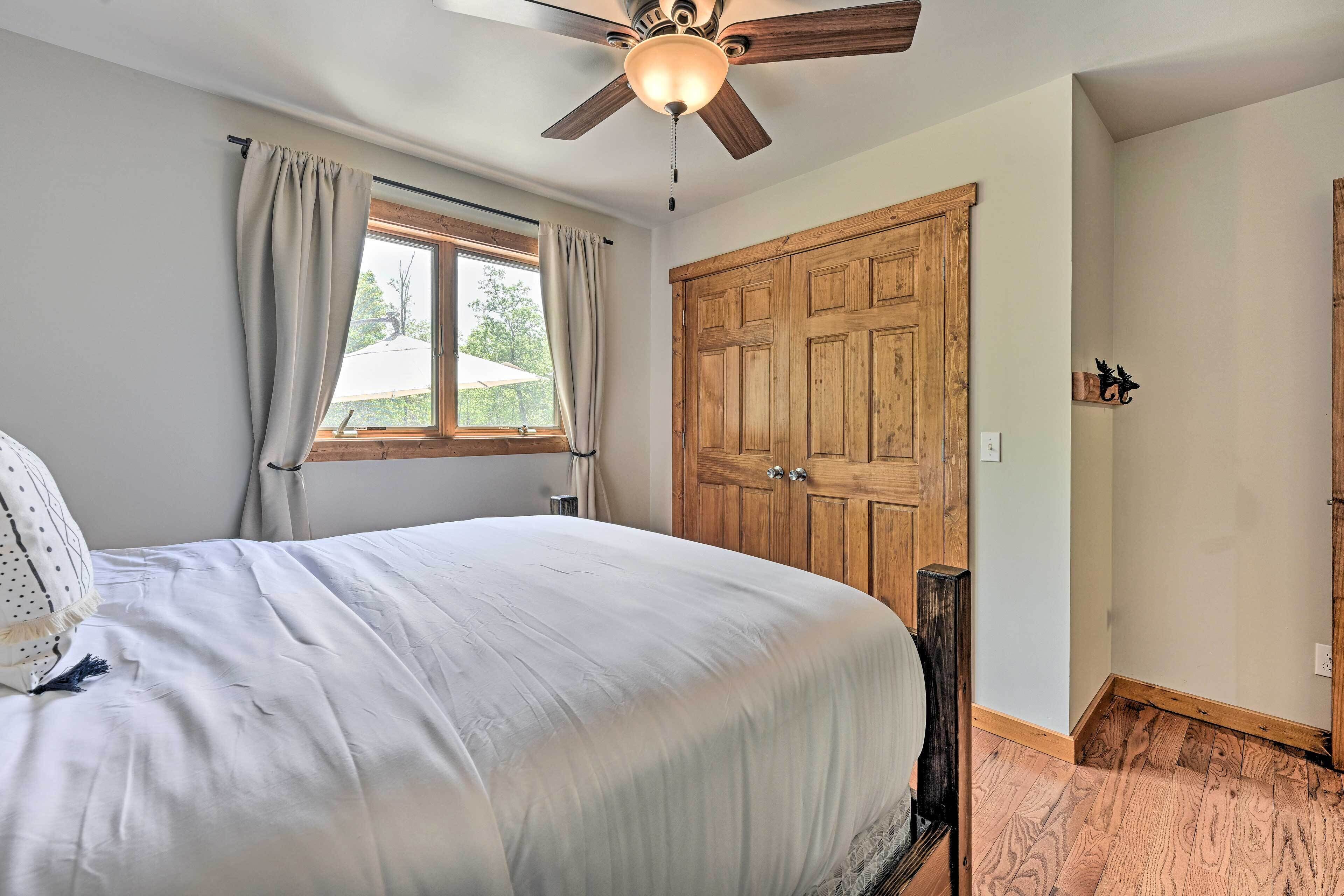 A bedroom with a large bed, a ceiling fan, a wooden wardrobe, and a window with curtains.