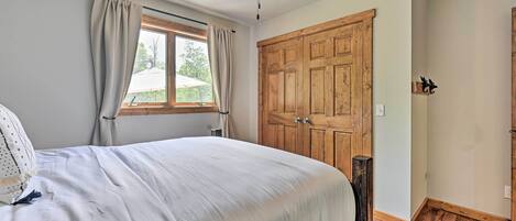 A bedroom with a large bed, a ceiling fan, a wooden wardrobe, and a window with curtains.