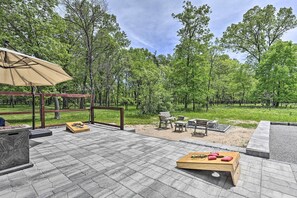 Un patio al aire libre con piso de piedra, mobiliario de madera y una pérgola con sombrilla color beige.