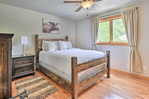 Un dormitorio con una cama de madera, una mesita de noche, una lámpara, una ventana con cortinas y un ventilador de techo.