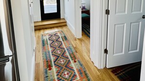 Un pasillo con alfombra estampada, suelo de madera, paredes blancas y una puerta que da a otra habitación.