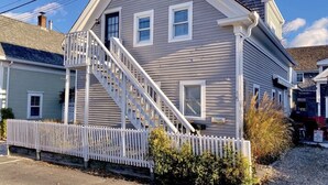 Una casa de dos pisos con una escalera blanca que lleva a la puerta principal, una cerca blanca en espiral y un cielo azul despejado.