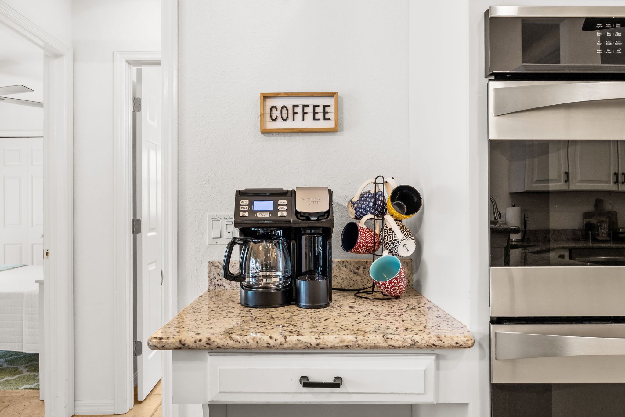 Eine Küche mit Kaffeemaschine, Tassen und einem Schild an der Wand mit der Aufschrift 'COFFEE'.