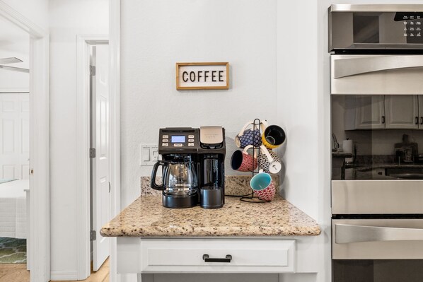 A kitchen with a coffee maker, mugs, and a sign that says 'COFFEE' on the wall.