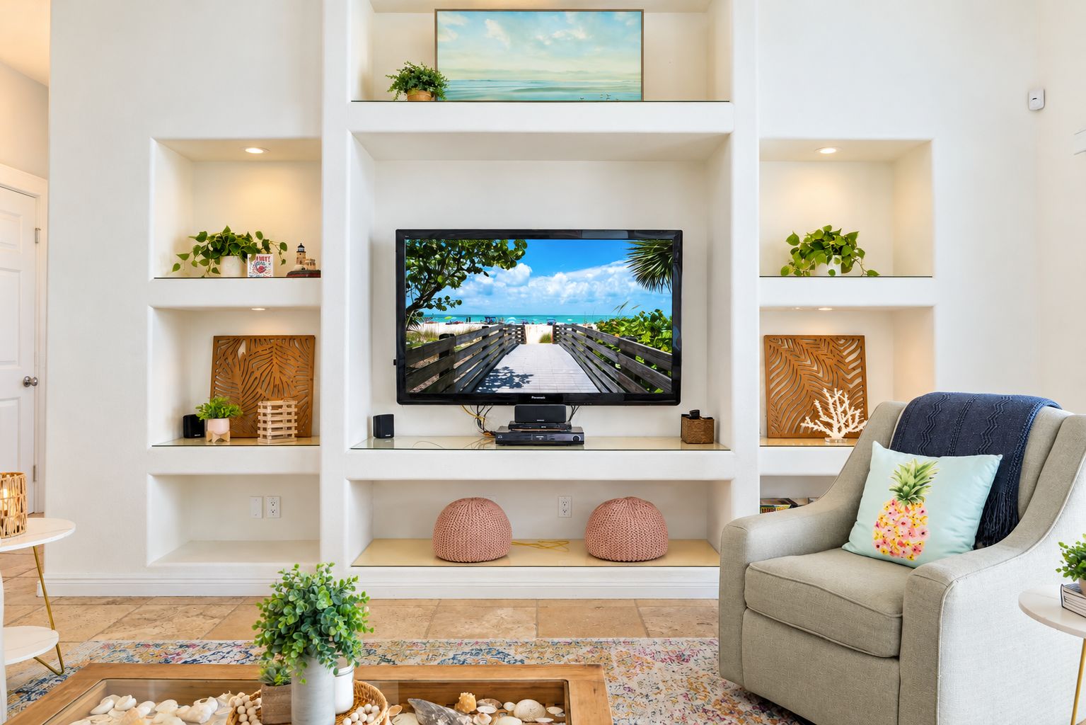 Ein Wohnzimmer mit einem an einer weißen Wand befestigten Flachbildfernseher, umgeben von Regalen mit Dekoration und Pflanzen.