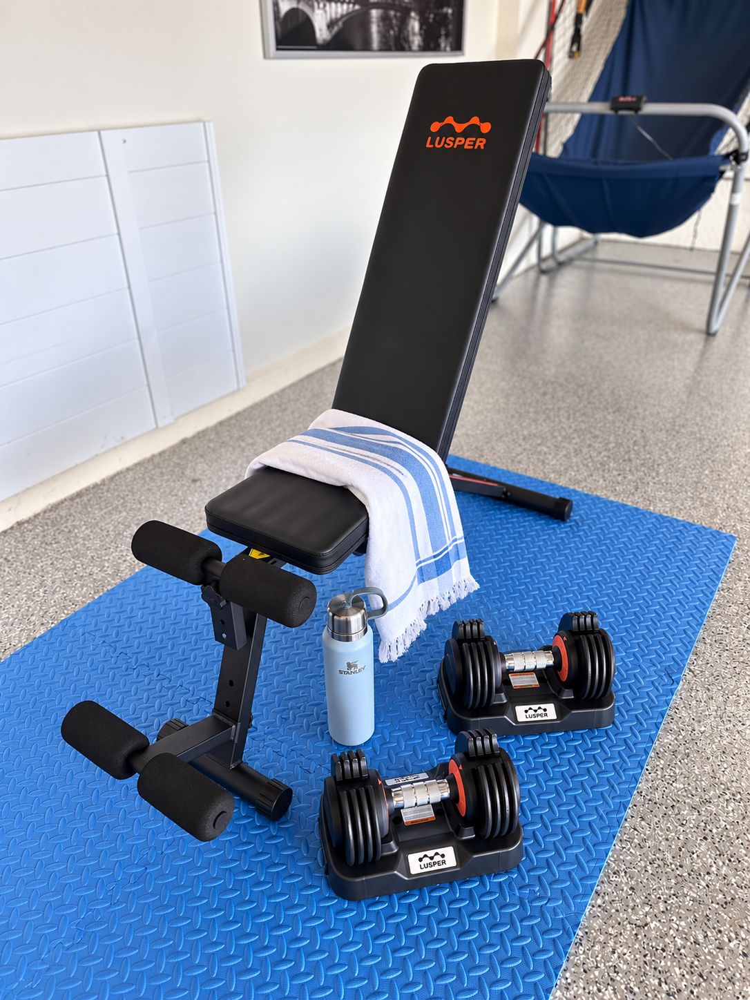 Un banc de musculation avec des haltères et une bouteille d’eau, le tout posé sur un tapis bleu.