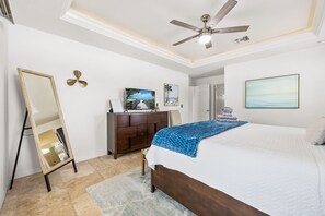 A bedroom with a bed, a ceiling fan, a dresser, a TV, and a painting on the wall.