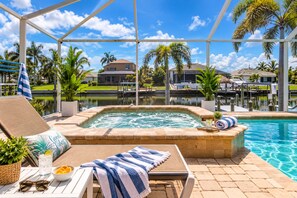 A poolside area with a hot tub, lounge chairs, and a view of a marina and houses.