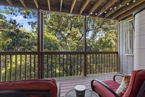 A covered outdoor area with a wooden deck, two chairs, a table, and a view of trees. - NEW! Walk-In Condo: 1 mi to SDC!, 2 Pools ~ Private Deck (Branson West)