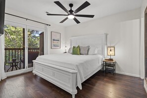 A bedroom with a large bed, a ceiling fan, a nightstand with a lamp, and a view through a sliding glass door to an outdoor deck.