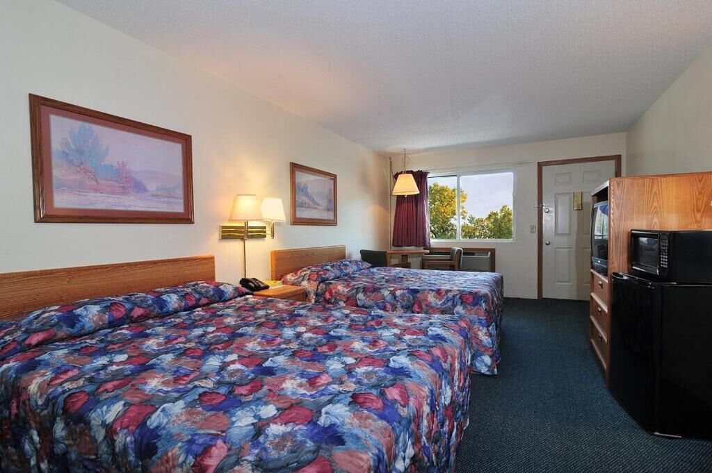 A hotel room with two beds, a desk, a chair, a lamp, a television, and a refrigerator.