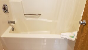 A white bathtub with a grab bar, a towel, and a wooden door. - Dells Park Motel (Wisconsin Dells)
