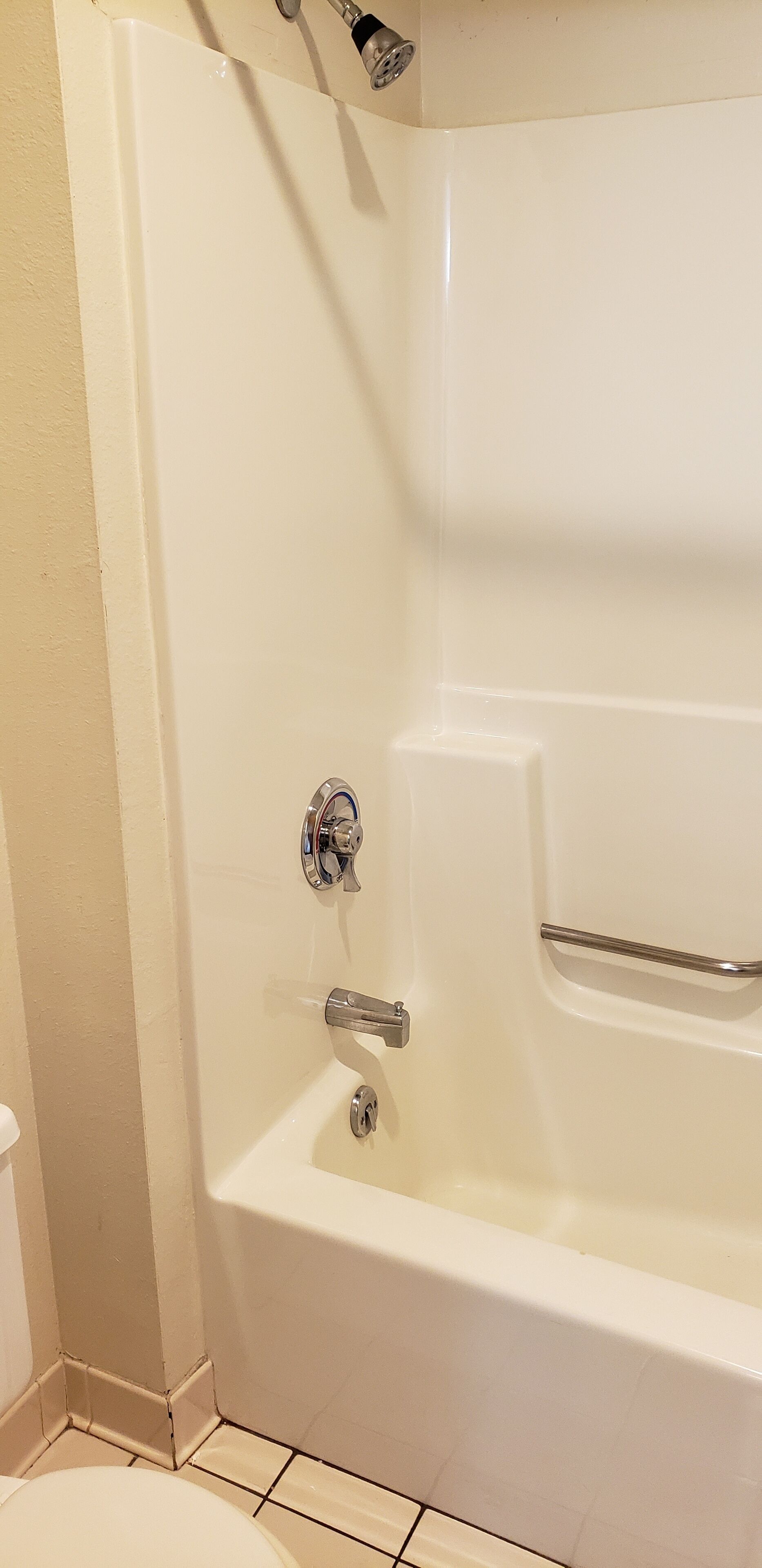A corner of a bathroom with a white bathtub, a showerhead, and a toilet.