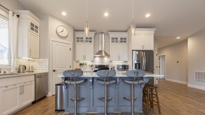 A modern kitchen with white cabinets, a stainless steel refrigerator, a microwave, and a bar area with stools. - Cozy new built home 10 minutes away from Portland (Vancouver)
