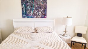 Una cama bien hecha con una colcha estampada, un cabecero blanco y una mesita de noche con una lámpara.