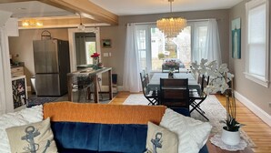 A modern living room with a blue sofa, a dining table, and a kitchen area with a refrigerator. - Right on the Cape Cod Canal and bike path! (Bourne)