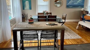 A dining area with a table, chairs, and a chandelier. There are paintings on the walls, a window with curtains, and a view of the ocean. - Right on the Cape Cod Canal and bike path! (Bourne)