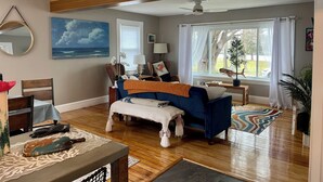 A spacious living room with a large window, a ceiling fan, and a view of the outdoors. - Right on the Cape Cod Canal and bike path! (Bourne)