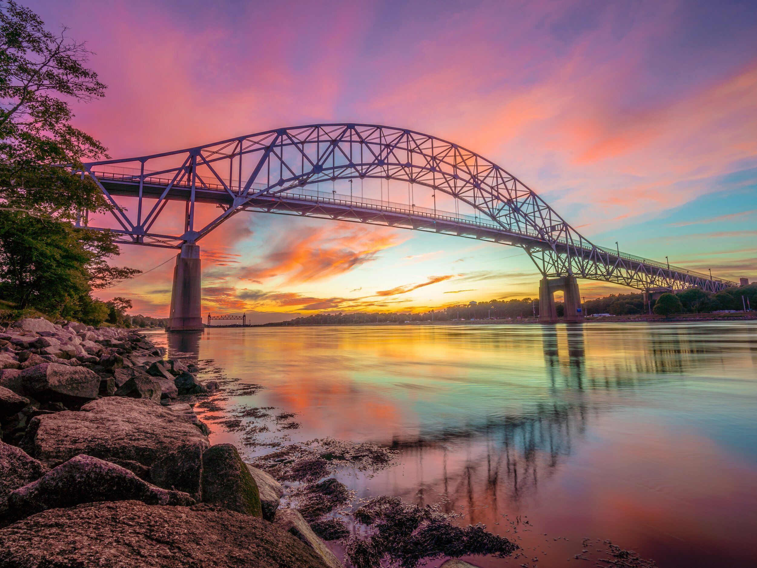 Un pont d’acier enjambant une rivière paisible au coucher du soleil.