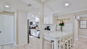 A modern kitchen with white cabinets, a central island with bar stools, a microwave, and a coffee maker. - Private Pool & Hot Tub - Minutes from Disneyland - Comfort & Convenience (Anaheim)