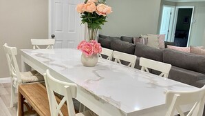 A dining area with a white marble table, white chairs, a bench, and a vase with flowers. - Private Pool & Hot Tub - Minutes from Disneyland - Comfort & Convenience (Anaheim)