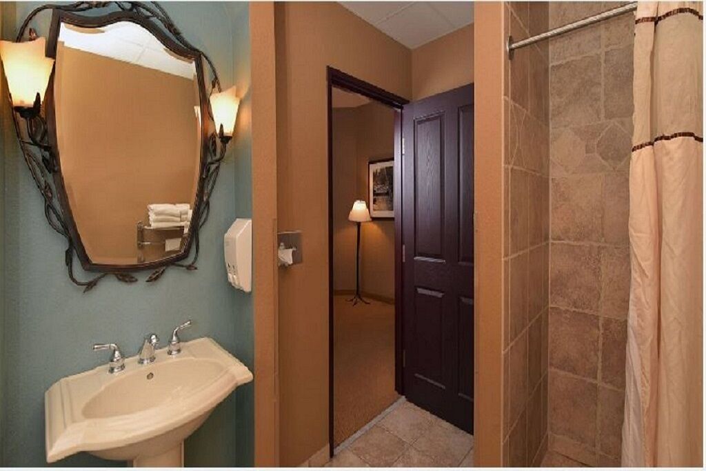 A bathroom with a large mirror, a sink, a door leading to another room, and a shower area.