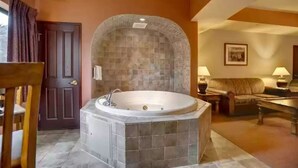 Una habitación con bañera de baldosas de piedra, una puerta, un sofá y una mesa con lámparas.