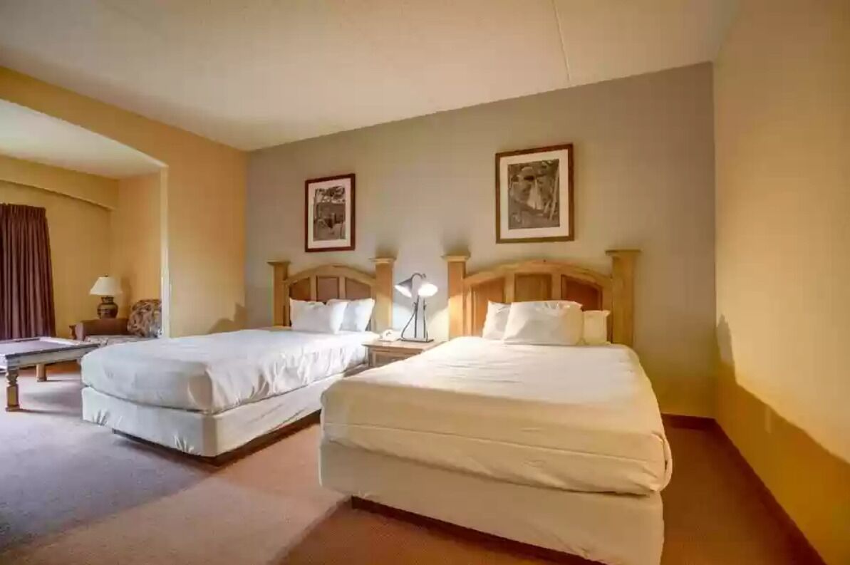 Een hotelkamer met twee enkele bedden, een bureau, een stoel en twee ingelijste foto's aan de muur.
