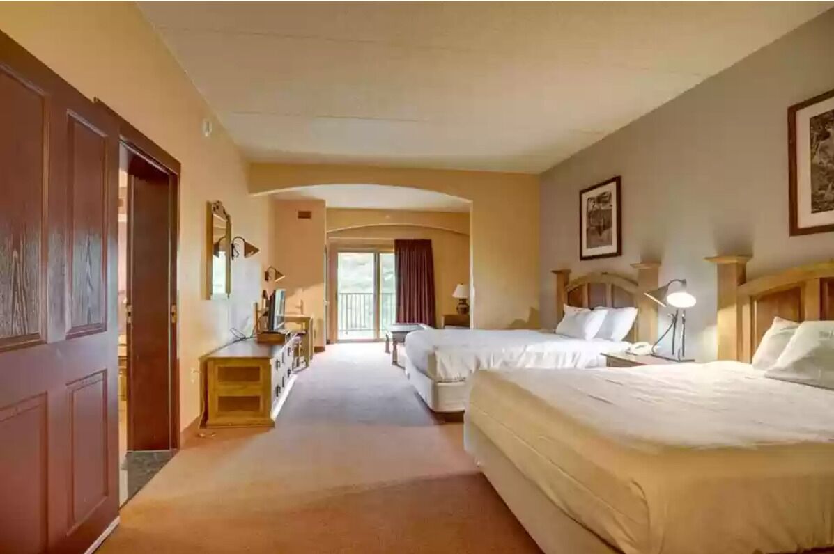 A hotel room with two beds, a desk, a chair, a lamp, and a window with curtains.
