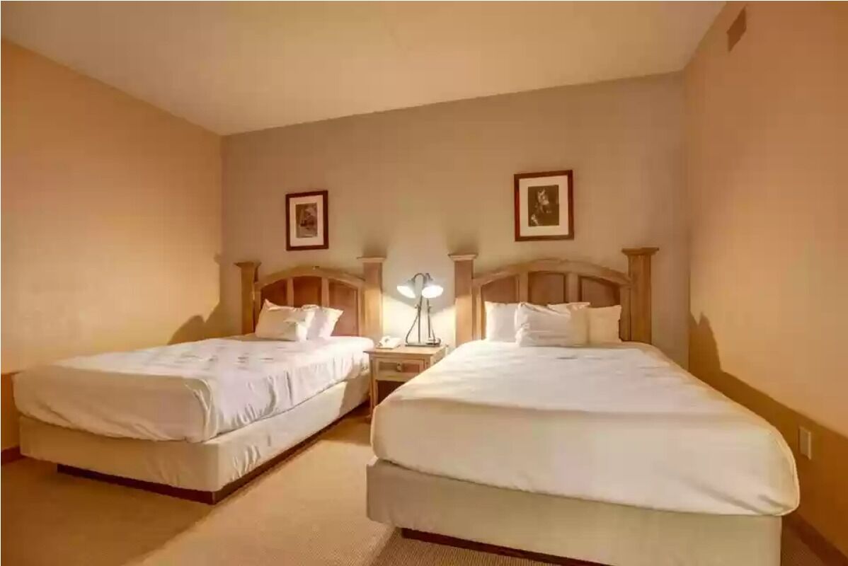 Une chambre d’hôtel avec deux lits simples, une table de chevet avec une lampe et un tableau accroché au mur.