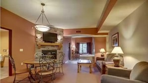 Una sala de estar con chimenea, televisor montado en la pared, una mesa de comedor con sillas y un sofá.