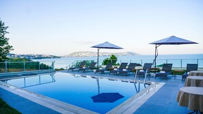 A pool area with lounge chairs and umbrellas, overlooking a cityscape and the sea. - Sinop Koru Hotel (Sinop)