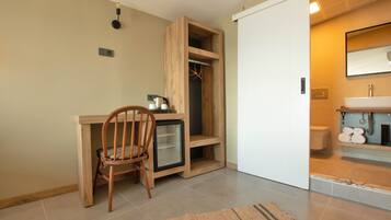 Habitación compacta con escritorio de madera, una silla, un refrigerador pequeño y un armario empotrado.