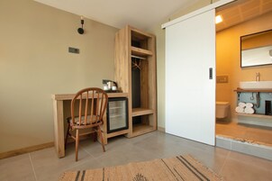 Habitación compacta con escritorio de madera, una silla, un refrigerador pequeño y un armario empotrado.