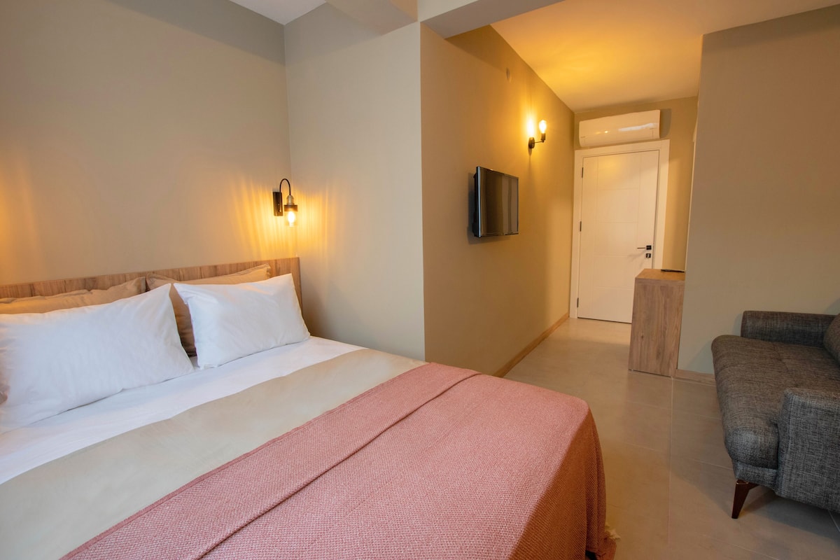 A hotel room with a bed, a chair, a TV mounted on the wall, and a door leading to another room.