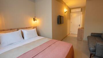 A hotel room with a bed, a chair, a TV mounted on the wall, and a door leading to another room.