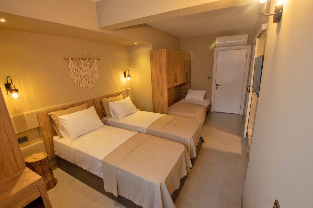 A hotel room with two single beds, wooden headboards, a wooden wardrobe, and a wall-mounted light fixture.