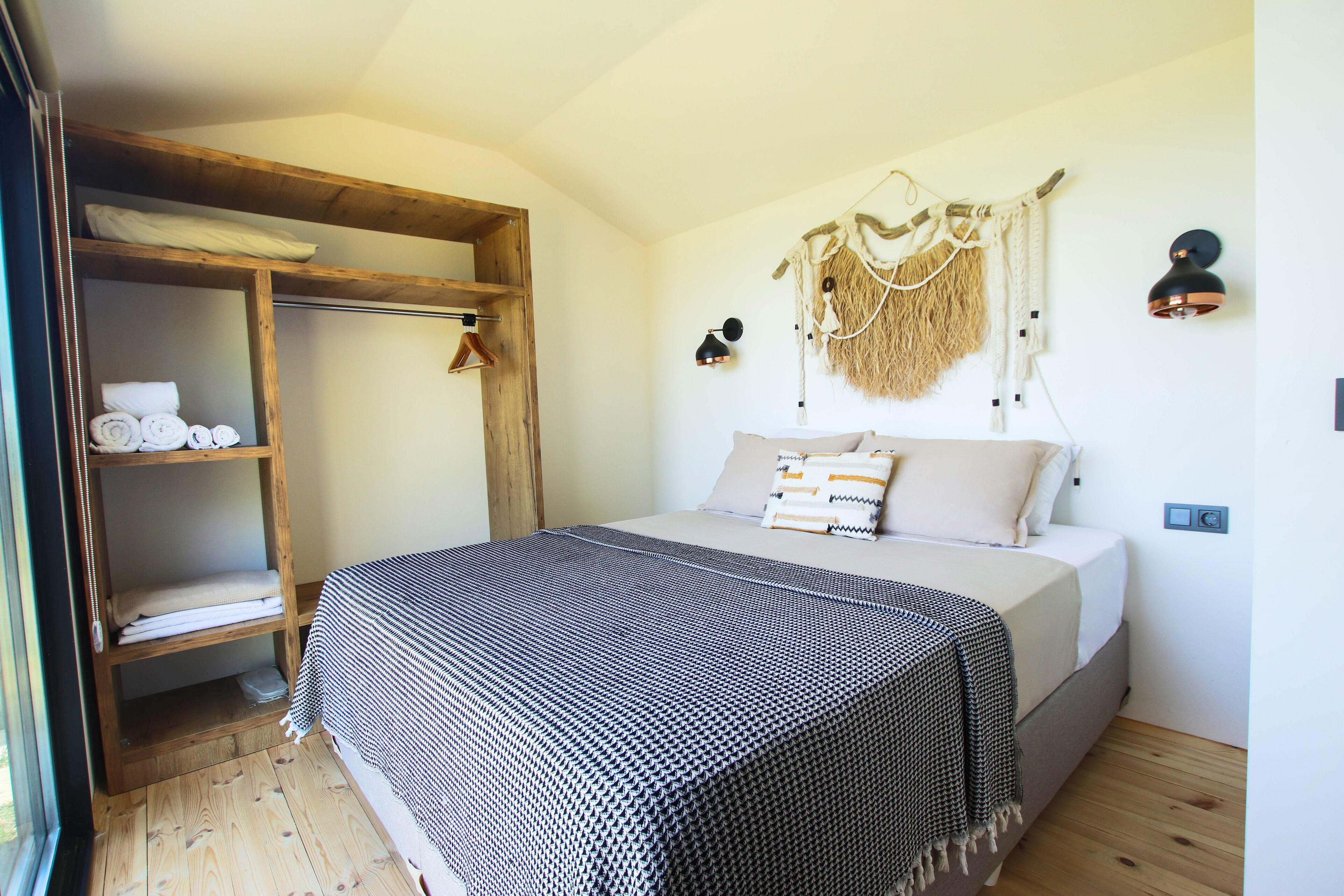 A bedroom with a bed, wooden shelves, a hanging wall decoration, and a wall-mounted lamp.