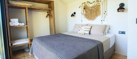 A bedroom with a bed, wooden shelves, a hanging wall decoration, and a wall-mounted lamp.