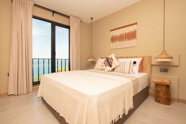 A bedroom with a large bed, a view of the sea through a sliding door, and a wooden headboard. - Sinop Koru Hotel (Sinop)