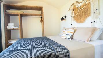 A room with a bunk bed, a wooden shelf with towels, a wall-mounted lamp, and a macrame wall hanging.