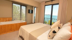 Un dormitorio con una cama grande, una bañera de madera y vistas al mar.